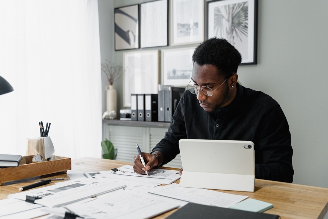 a person at a desk with an ipad writing on some papers